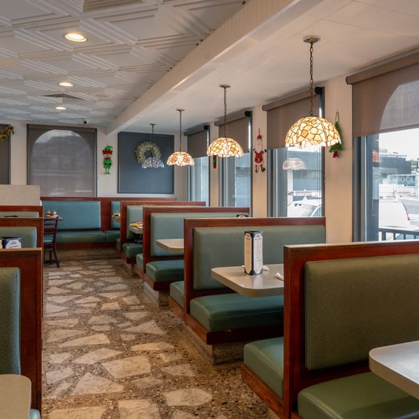 Interior of Frankie's Diner with rows of empty green booths, tables, and decorative stained-glass lamps.