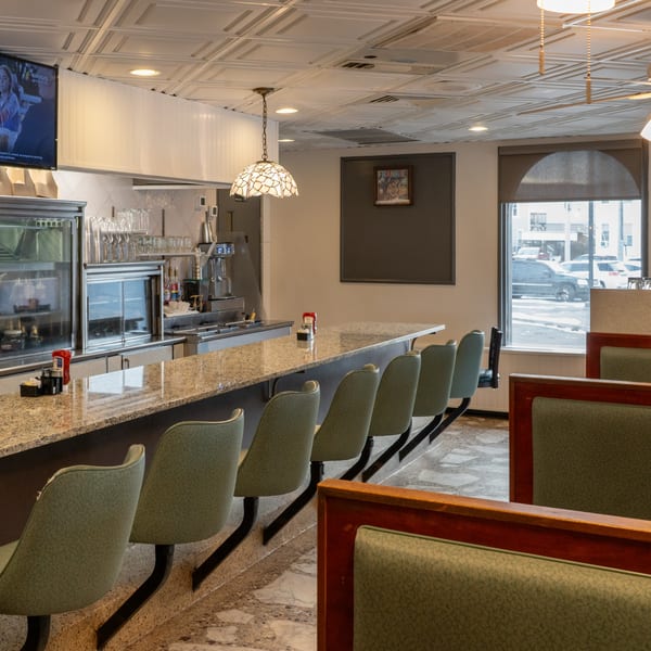 Interior of Frankie's Diner with a long counter, bar stools, booths, and a street view.