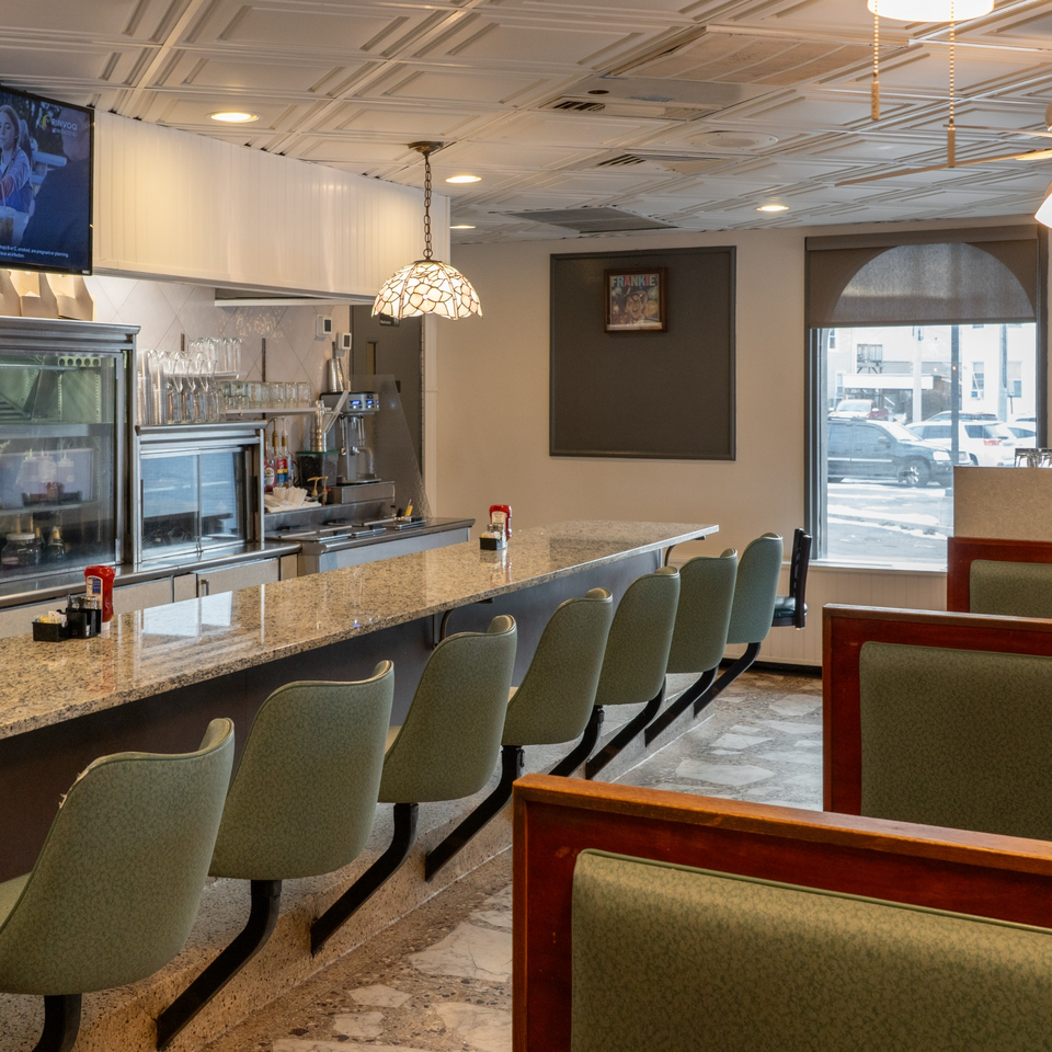 Interior of Frankie's Diner with a long counter, bar stools, booths, and a street view.