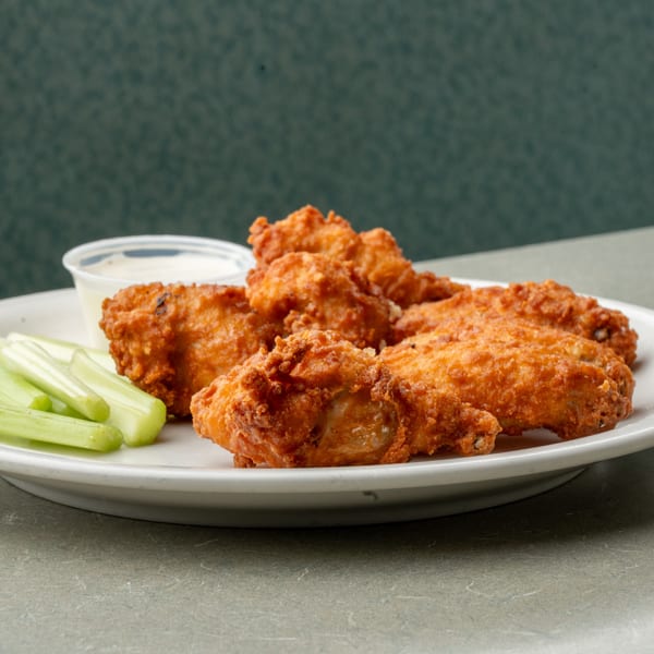 Crispy fried chicken wings with celery sticks and a side of ranch dressing on a white plate.