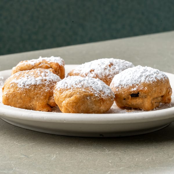 A plate of golden-brown fried dough balls, generously dusted with powdered sugar, at Frankie's Diner.
