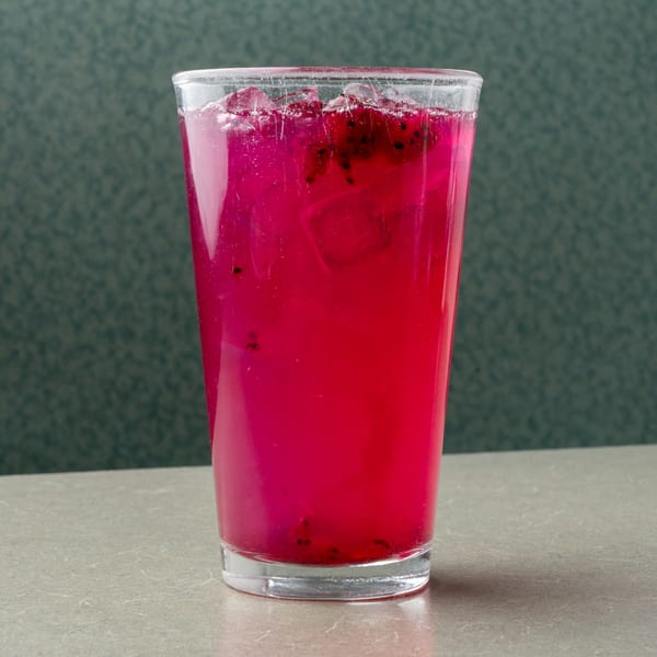 Vibrant pink dragon fruit drink with ice in a clear glass on a diner table.