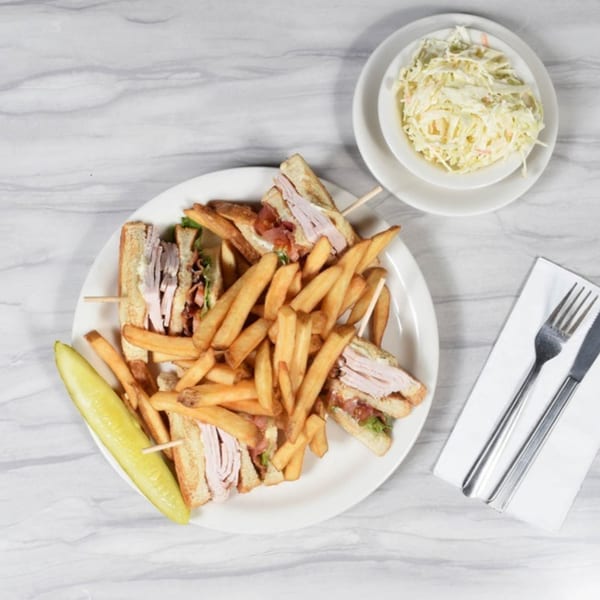 Frankie's Diner club sandwich with fries and a pickle, served with a side of coleslaw.
