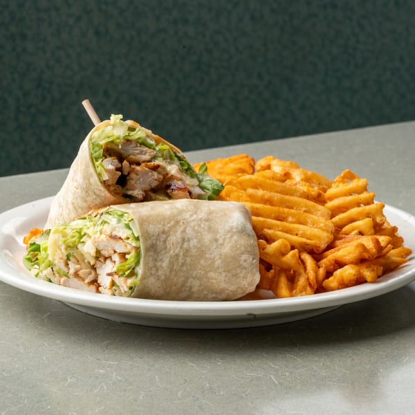 Two chicken wraps with lettuce and waffle fries on a white plate at Frankie's Diner.