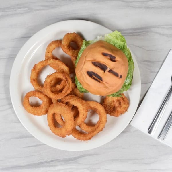 A grilled chicken sandwich with lettuce and a side of crispy onion rings on a white plate.