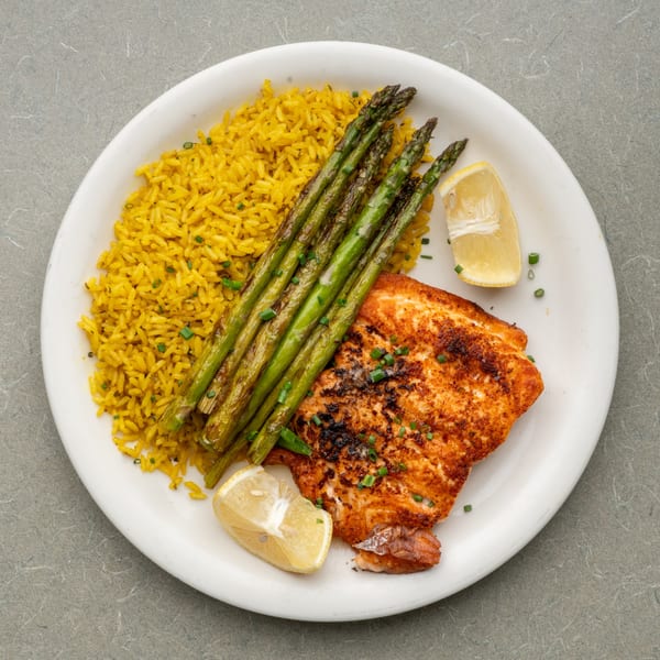 Frankie's Diner salmon with yellow rice, grilled asparagus, and lemon wedges on a white plate.