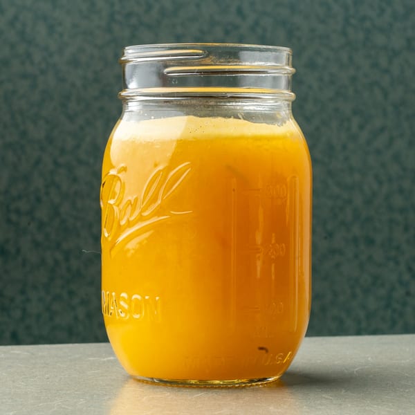 Bright orange juice in a Ball Mason jar on a gray counter with a dark green background.